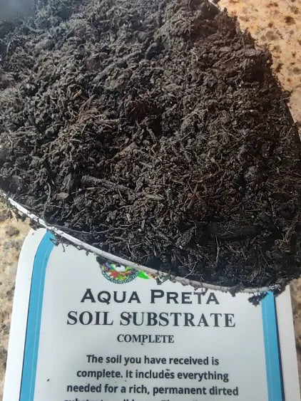 Scoop of Aqua Preta natural aquarium substrate in a silver scoop with Aqua Preta label in the background.